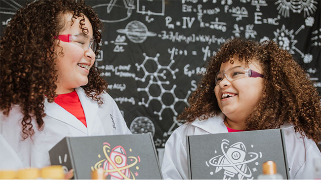 Two smiling children holding STEM boxes